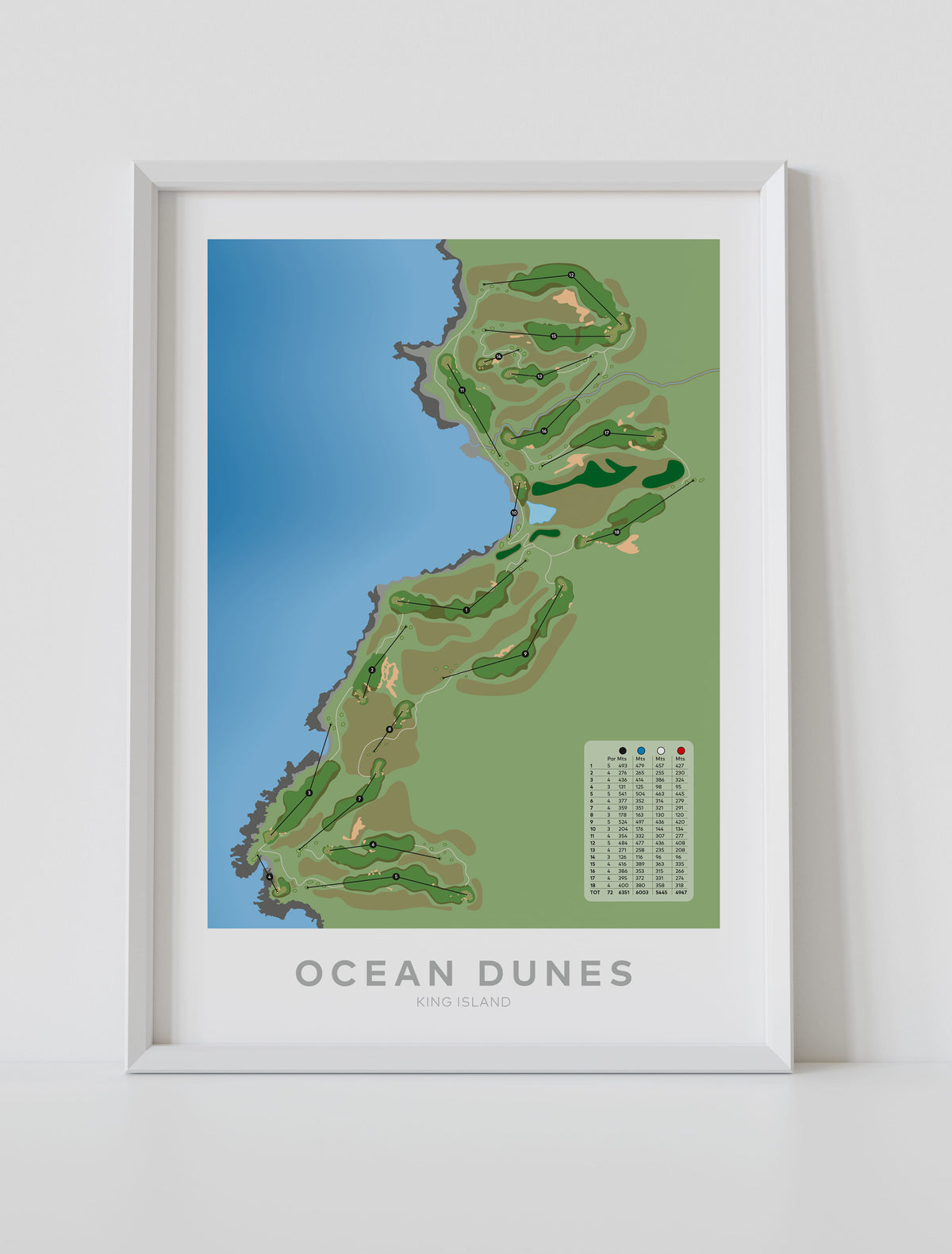 A framed golf course map print of Ocean Dunes King Island, featuring a stylized green and brown course layout next to blue water, displayed in a white frame on a light gray wall.-australia-golf-art