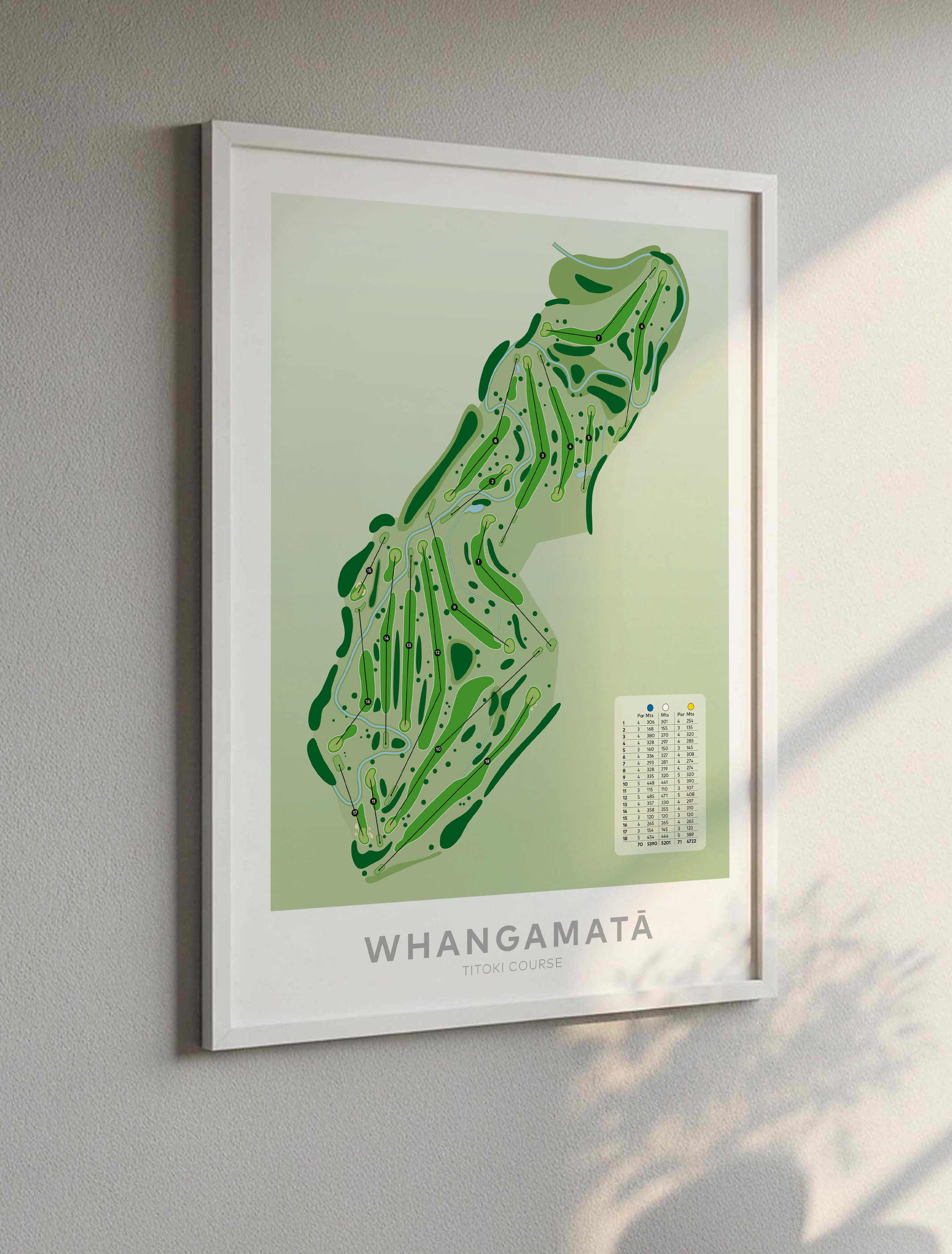 White framed art print featuring a green golf course map labeled 'WHANGAMATA' on a light gray wall, with soft sunlight casting shadows on the right side.